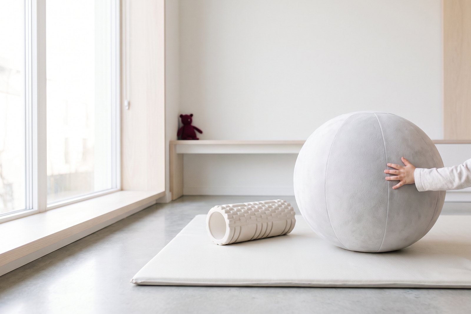 A child's hand resting on a soft ball beside a foam roller in a paediatric therapy room
