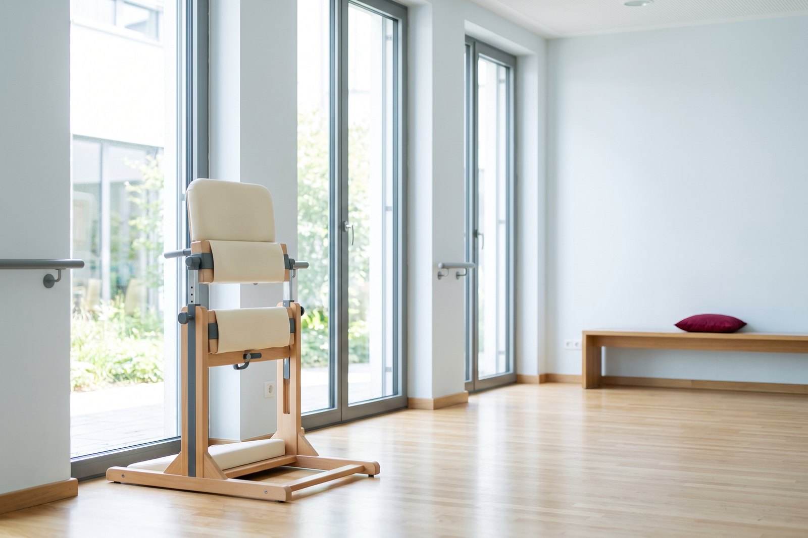 A standing frame beside tall windows in a bright rehabilitation hall