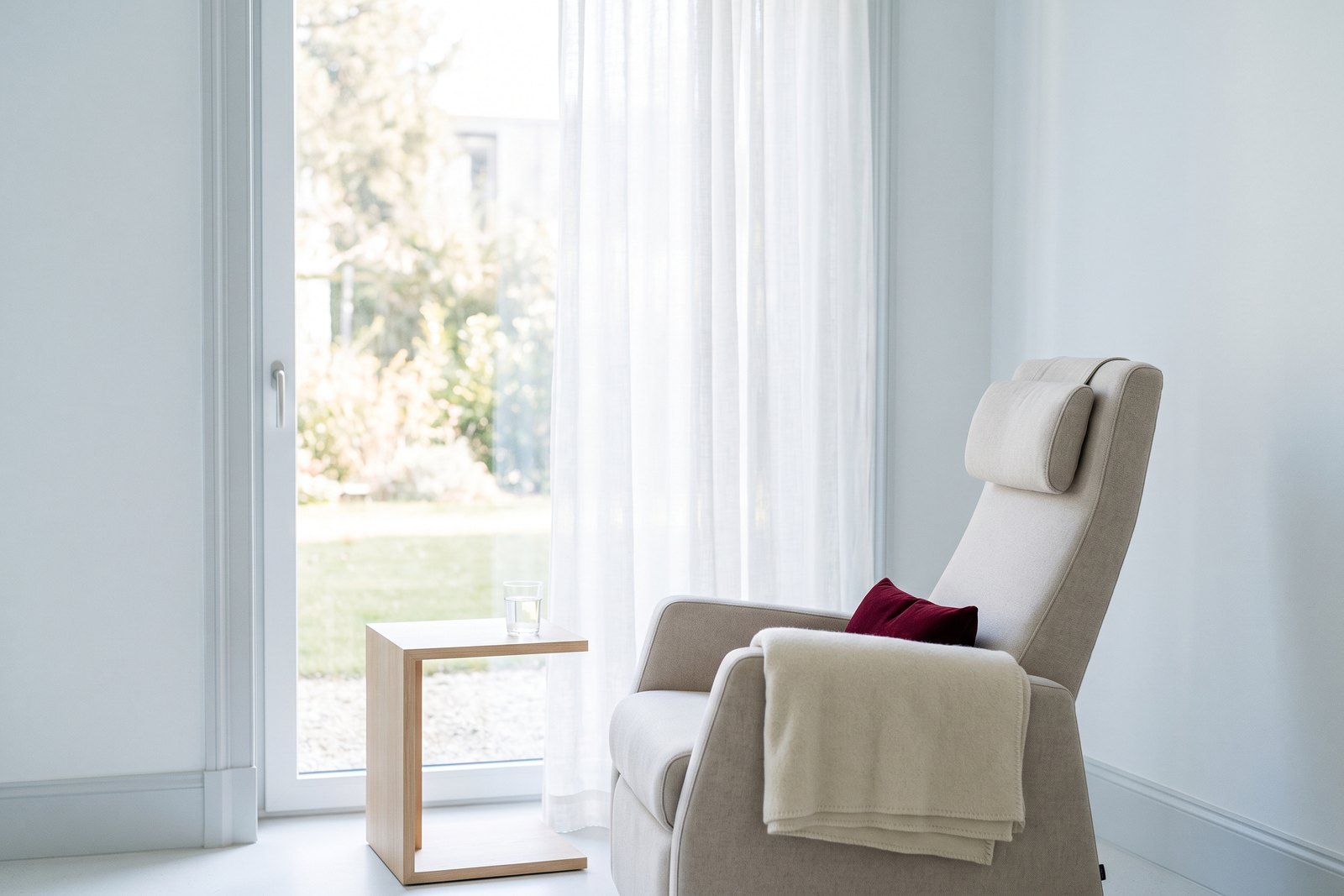 A reclining chair with a headrest and a wool blanket beside a tall window