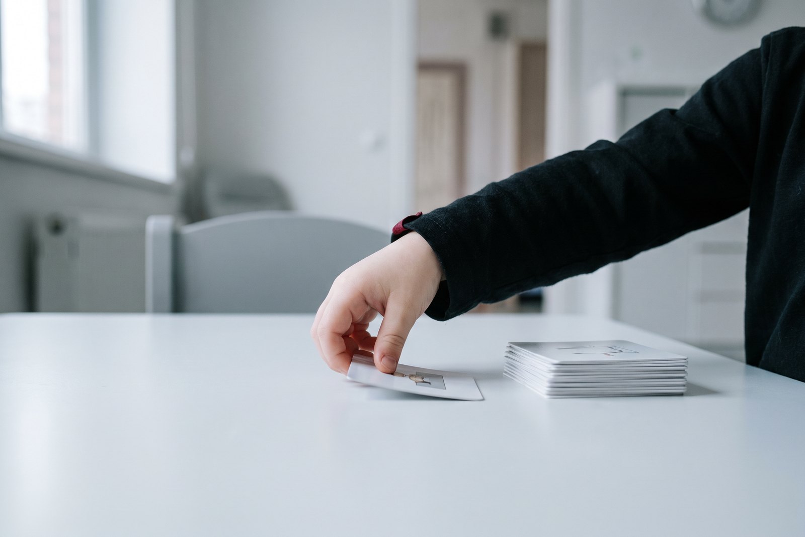 A child's hand placing a picture-communication card on a pale table