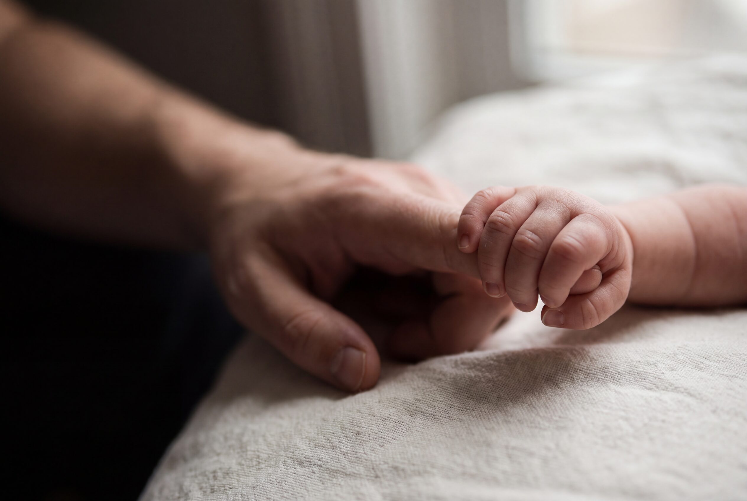 A newborn's hand closed around an adult's finger