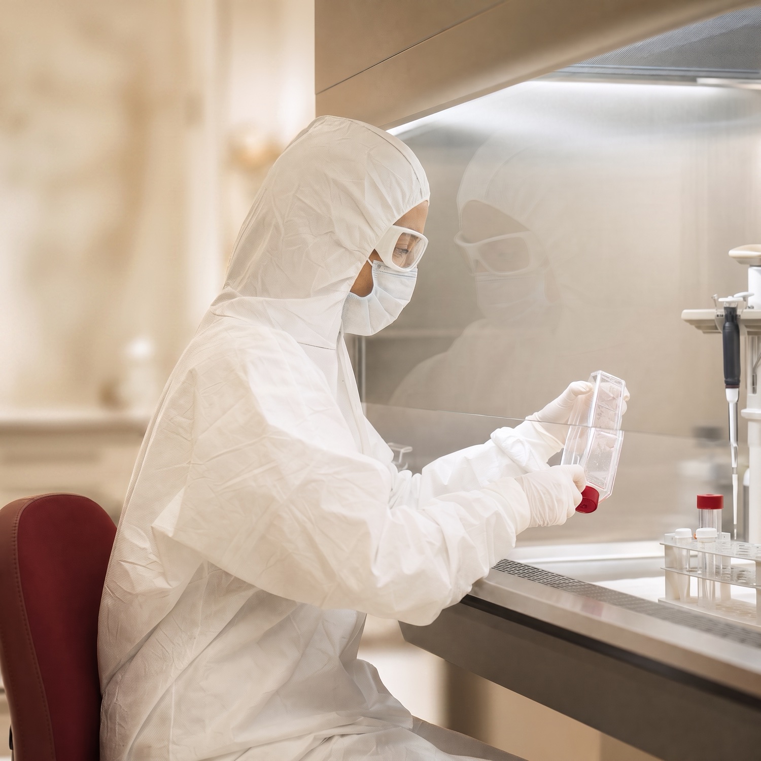 A scientist in full sterile cleanroom gown, mask and goggles preparing a culture flask of cells at the group's laboratory