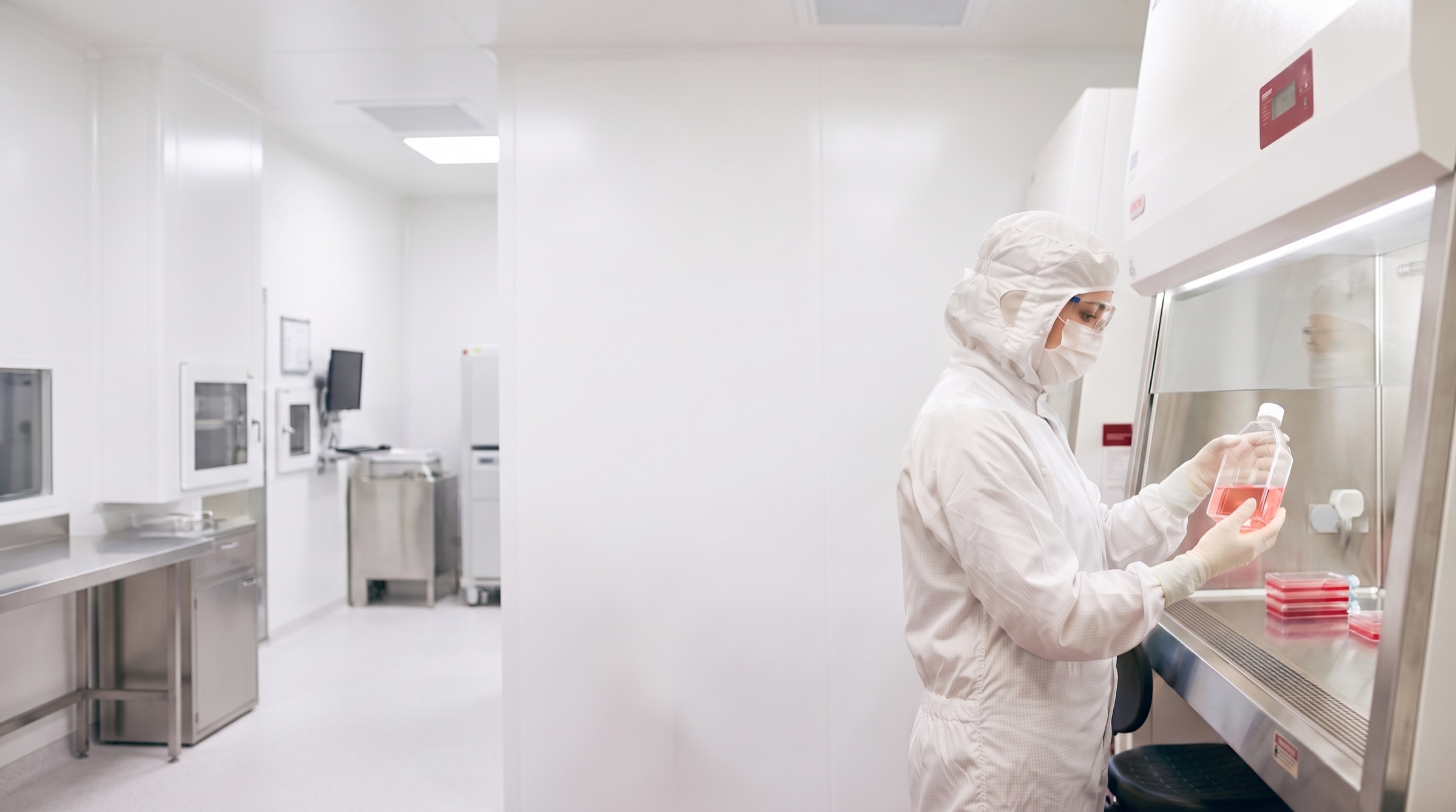 Una ricercatrice in camice sterile completo tiene in mano una fiasca di coltura nel laboratorio certificato del gruppo