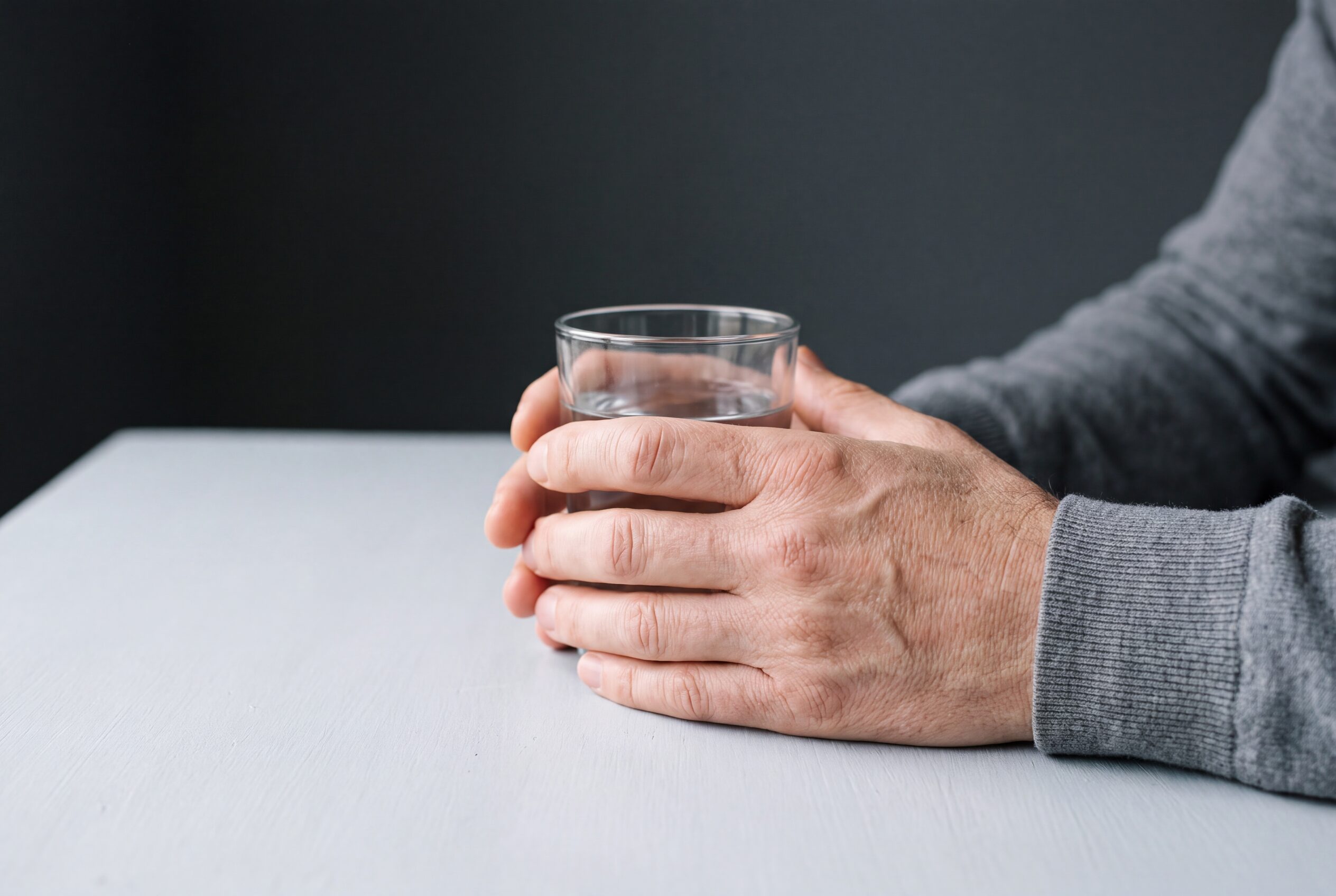 Both hands of an adult cupped around a glass of water on a table