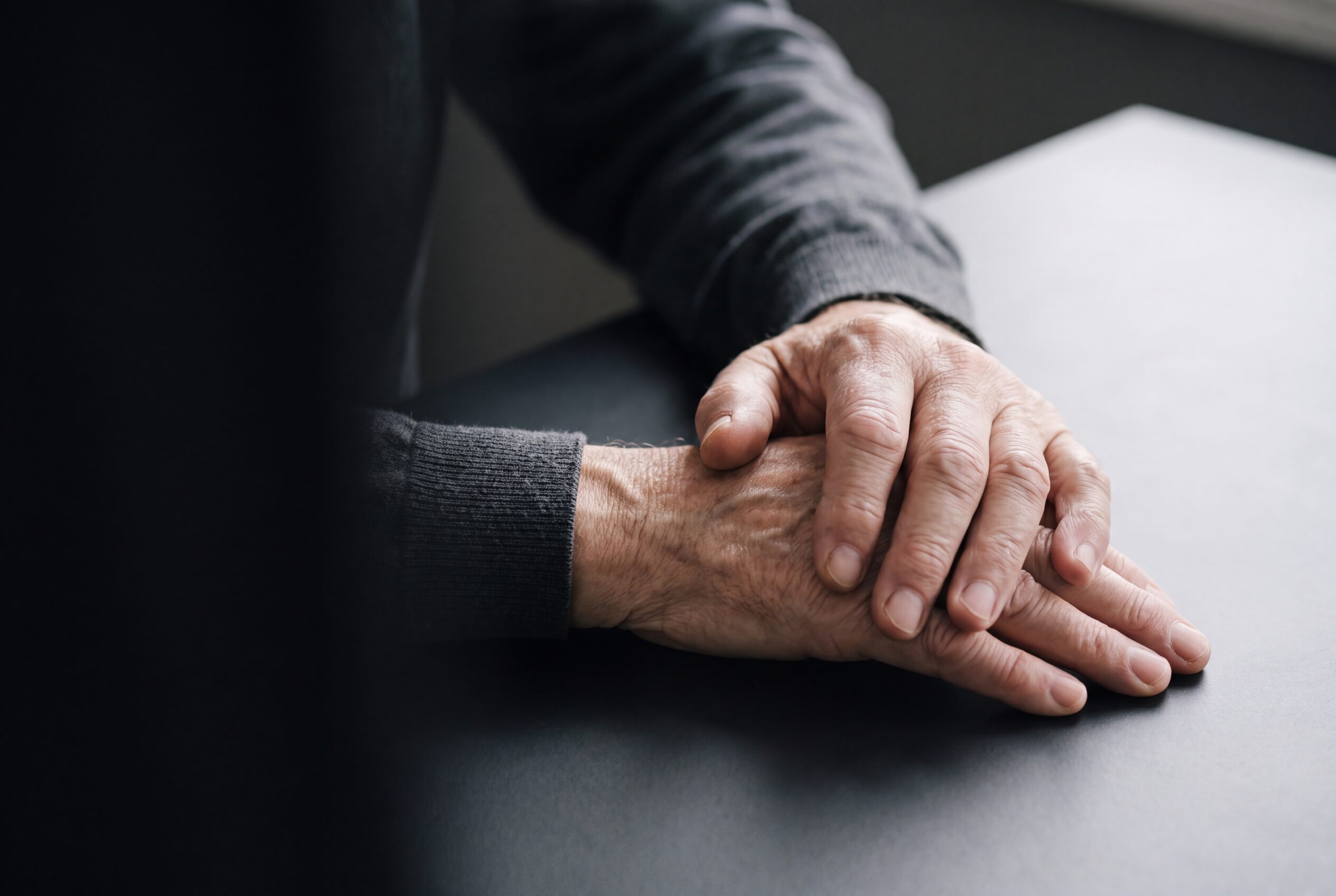 An older person's hands at rest on a table, one hand steadying the other